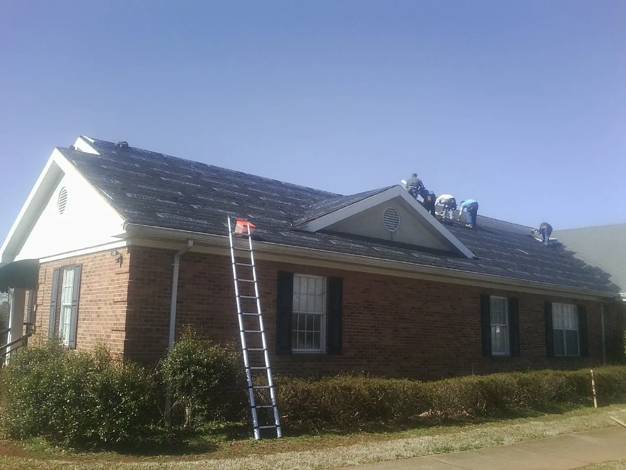 Crew tearing shingles off a brick ranch roof with a ladder set — Metal Roof Repair work by our crew in Brownsburg