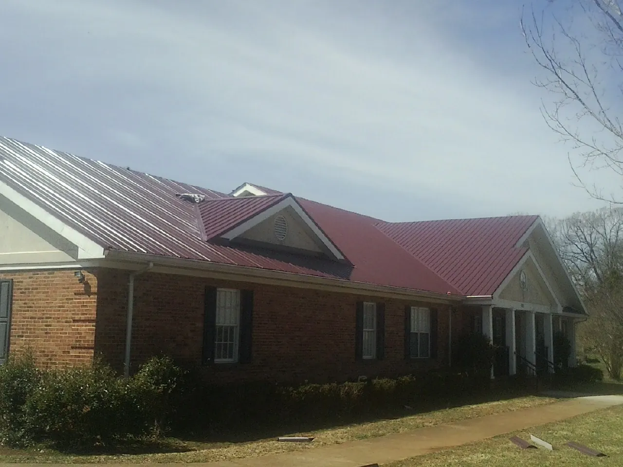 Red metal roof with gabled entries on a long brick building, from a Hail Damage Roof Repair job in Brownsburg