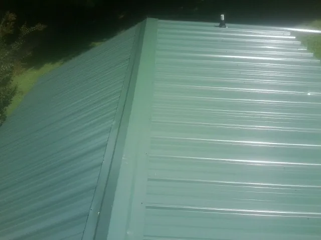 New green metal panels meeting at the ridge of a roof — Flat Roof Repair work by our crew in Brownsburg