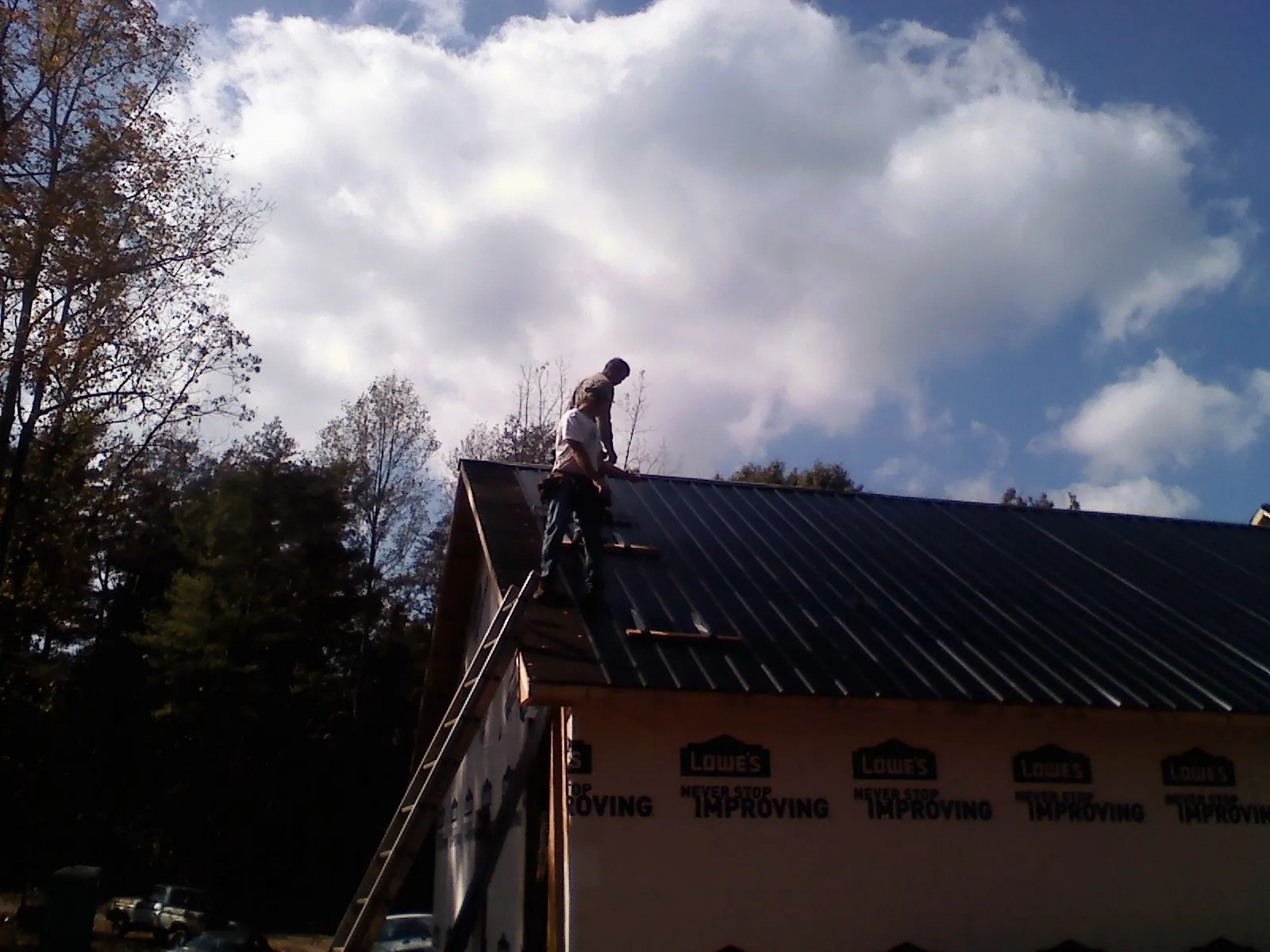 Roofer fastening dark metal panels high against a cloudy sky, from a Roof Inspection job in Brownsburg